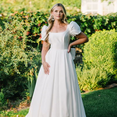 Bride wearing a mikado modest wedding dress with poufs sleeves and box pleats
