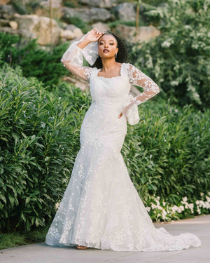 Beautiful posing with her hand turned up on her forehead. She is wearing and long sleeve modest wedding dress that has a three dimensional leaf pattern throughout the dress.