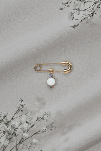 A basic shot of a "something blue" pin featuring gold details and a round white gem.