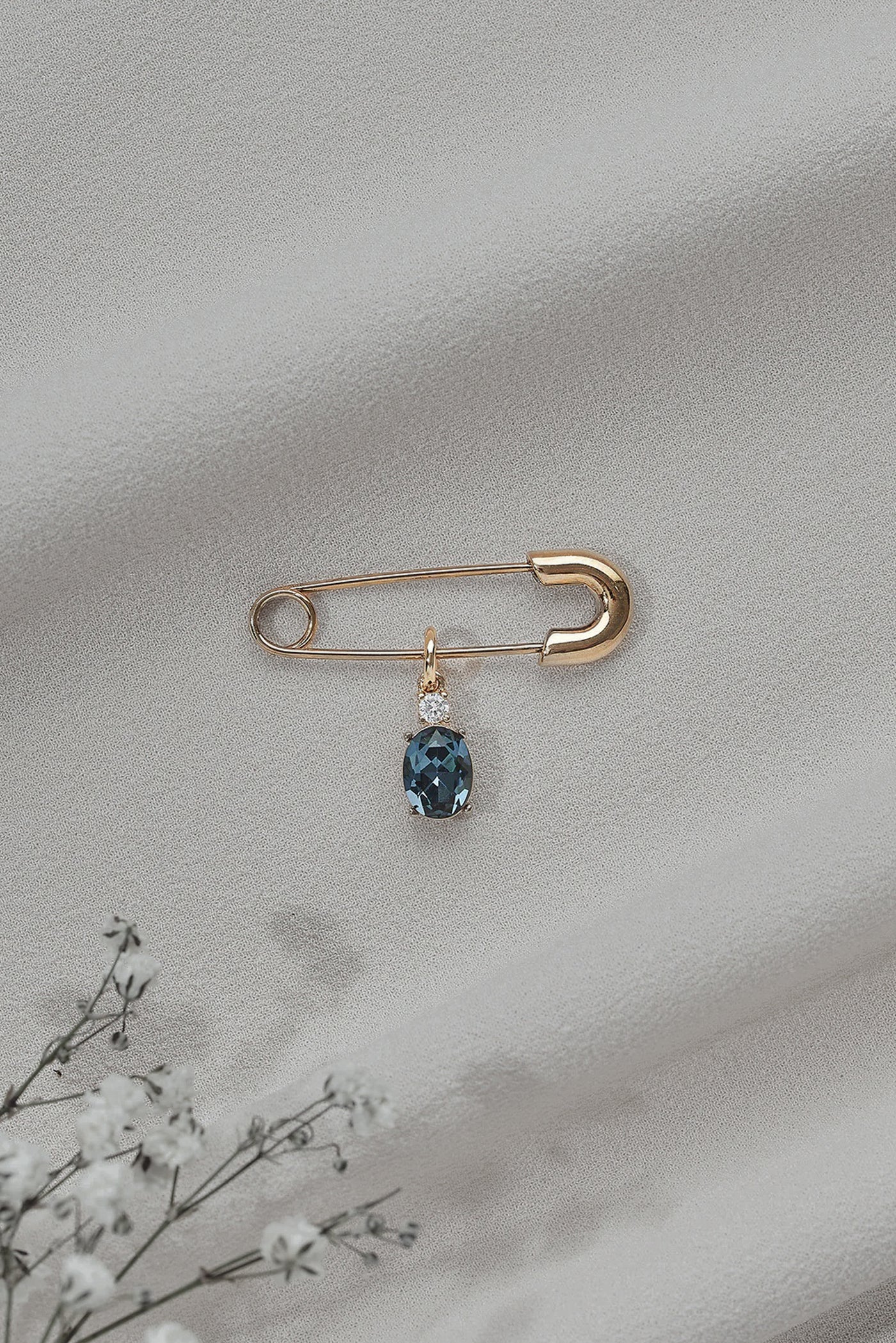 A basic shot of a gold safety pin with a blue gem attached to it.