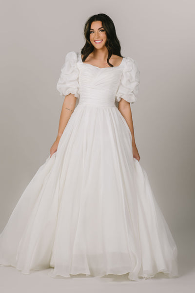 This is a front shot of a modest wedding dress with a ruched bodice and fun puff sleeves and ballgown silhouette.