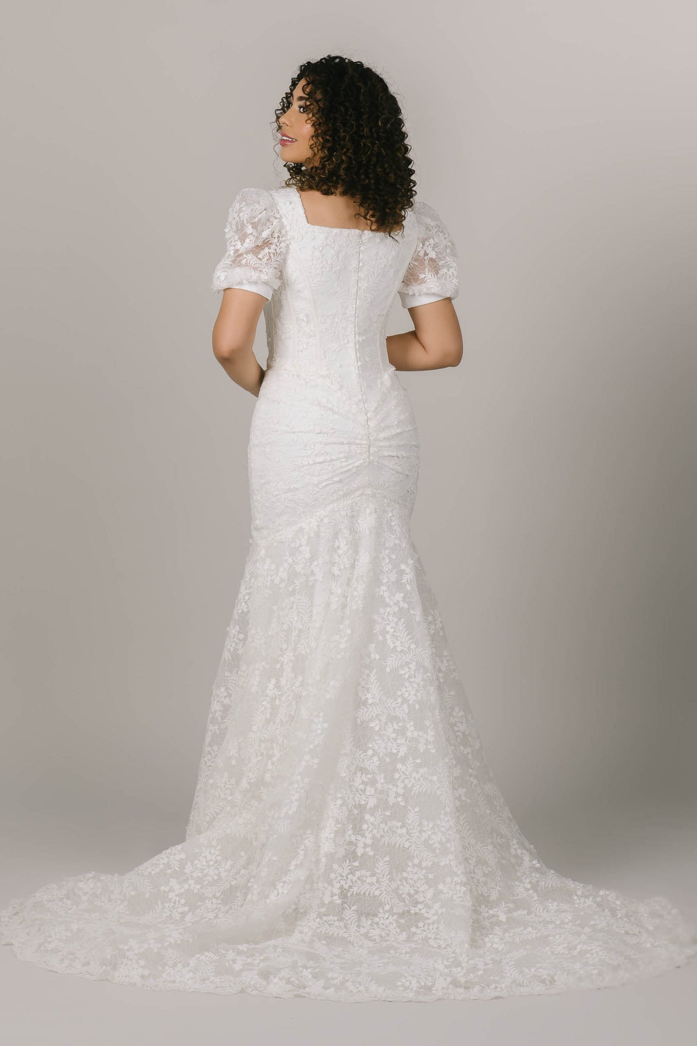 This is a back shot of a modest wedding dress with a mermaid silhouette and lacy long train.