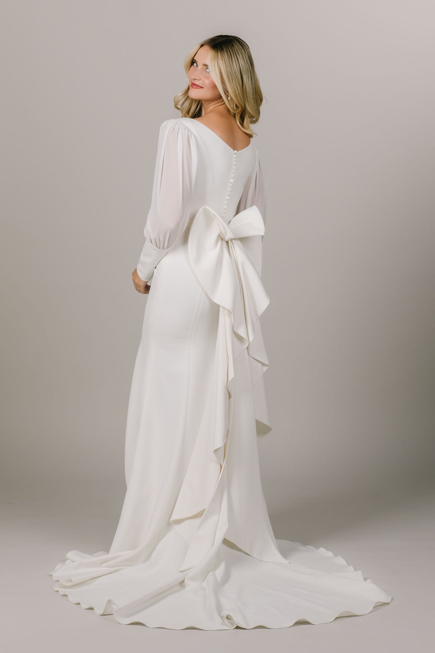 This is a back shot of a modest wedding dress with a fun bow on the back and sheer chiffon sleeves.
