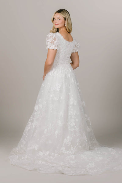 This is a modest wedding dress with a floral lace train and puff sleeve.