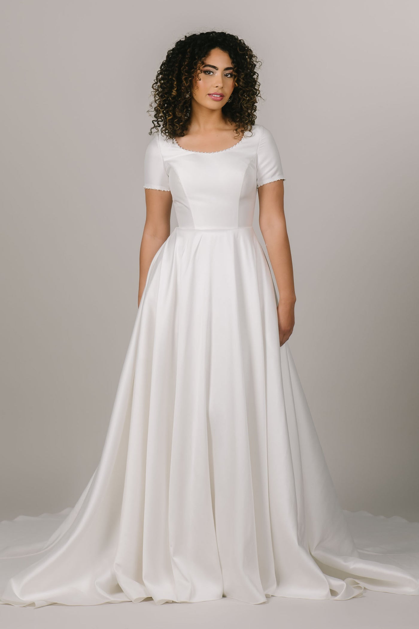 This is a front shot of a white modest wedding dress with pearl beading along the neckline and sleeves.