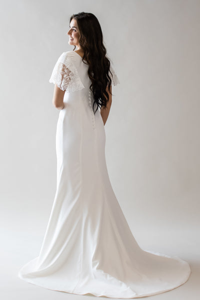 This is a brunette model wearing a white modest wedding dress with lace flutter sleeves and buttons along the back.