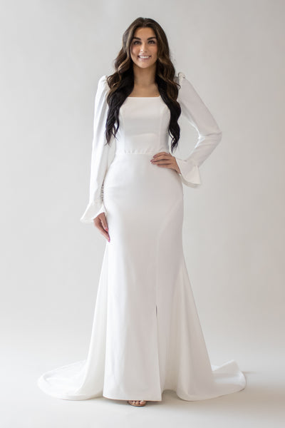 This is a white modest wedding dress with a square neckline, bell sleeves, and a slit down the front.