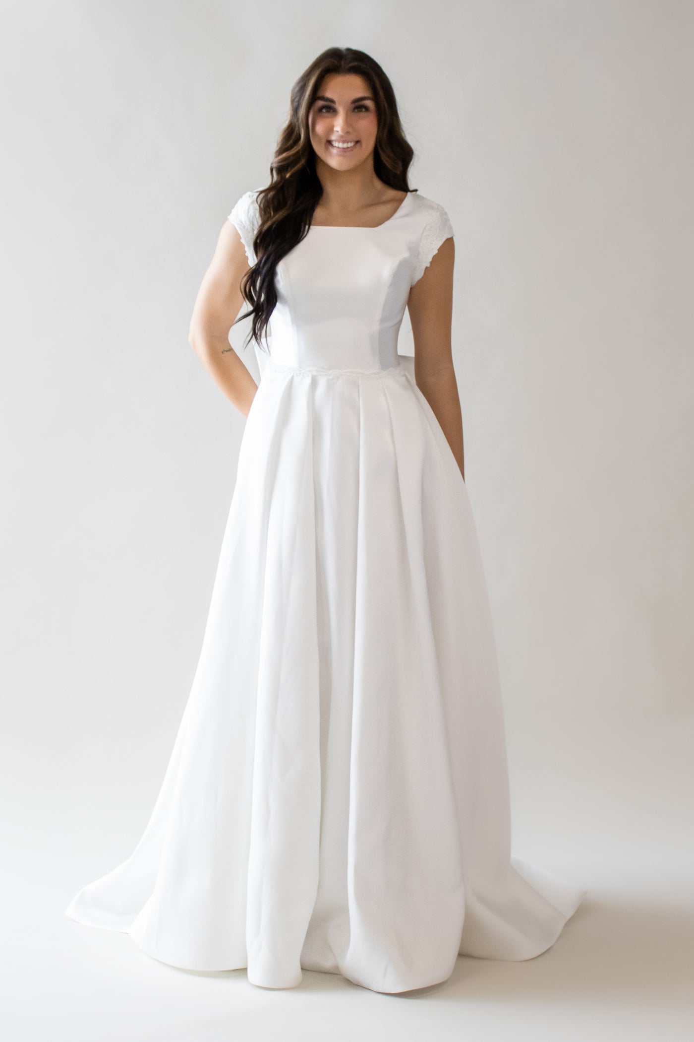 This is a modest wedding dress with an a-line skirt and pearl trip details.