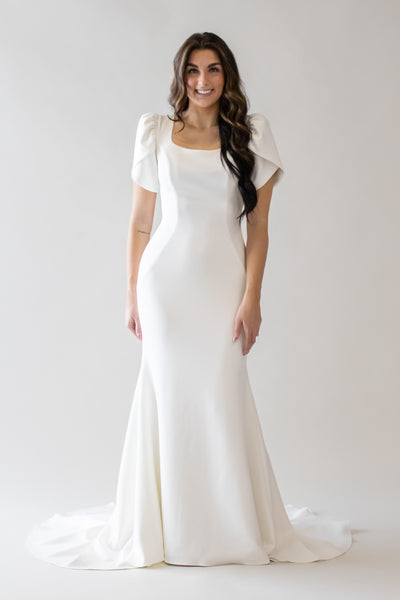 Sleek modest wedding dress with a soft square neckline. If you are looking for something modern, this is your dress! The beautiful petal puff sleeves are not only fun, but practical and allow movement. it can be dressed up with a unique veil or headpiece.