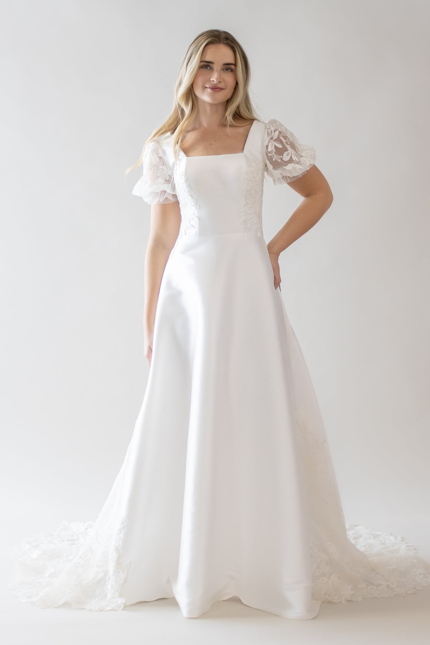This is a modest wedding dress with a shear lace puff sleeve, square neckline, and an a-line silhouette.