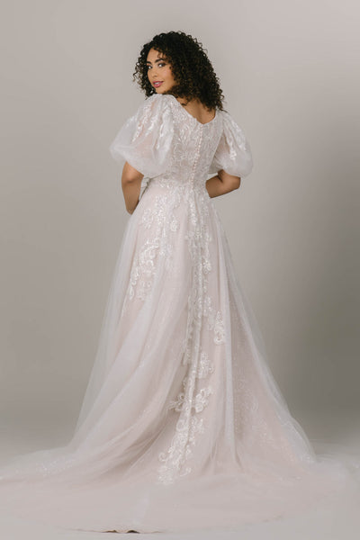 This is a back shot of a princess-y modest wedding gown with a sparkly layer and puff sleeves.