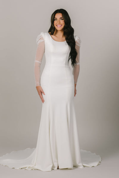 This is a front shot of a modest wedding gown with sheer sleeves and fitted silhouette.