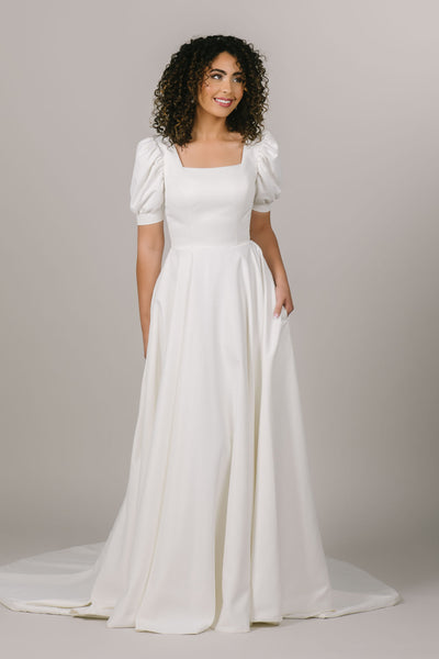 This is a front shot of a modest wedding gown with a square neckline and puff sleeves and a-line silhouette.