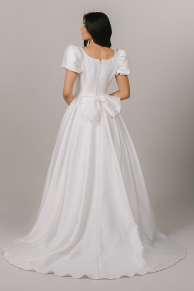 This is a back shot of a modest wedding dress with a fun bow on the back and buttons going all the way down.