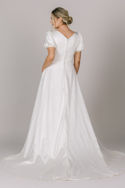 A back angle of a stunning modest wedding dress in Utah made out of the silky material of our dreams! It features a back v-neckline, soft puff sleeves, and buttons that go all the way down the gown.