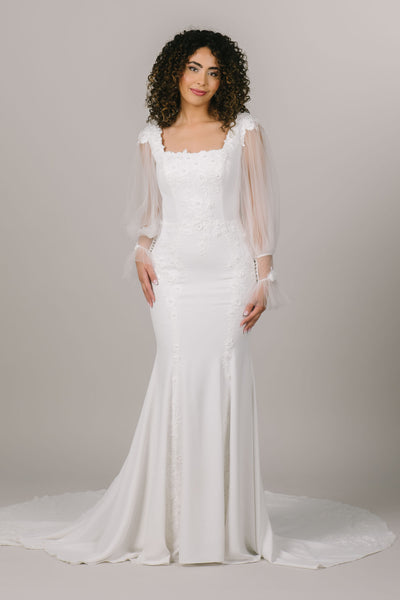 This is a front shot of a modest wedding dress with lace detailing all over the dress and long sheer sleeves.