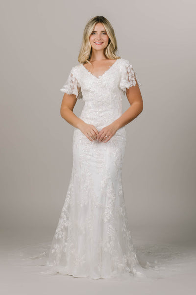 This is a sparkly flowery modest wedding dress with flutter sleeves and a slight mermaid silhouette. 