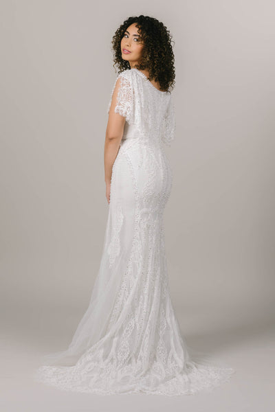 This is a back shot of a modest wedding gown with intricate beading and lace. There is a train that is also intricate.