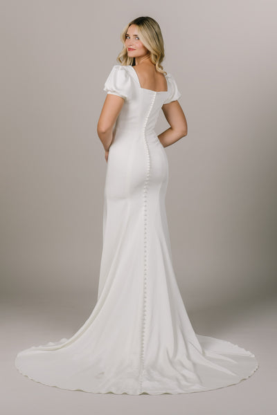This is a back shot of a modest wedding dress with a square back, buttons all the way down, and a puff sleeve.
