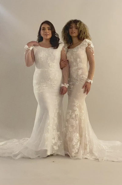 A video of a model on the left has a white tone and the model on the right has a nude color. The modest wedding dress has illusions flowers and leaves and this is a fit and flare dress silhouette.