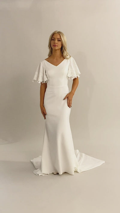 Video of sleek and modern flutter sleeve gown. The flutter sleeves have lace on the edge. This modest wedding dress is fitted and has a v-neckline. Moments Made Bridal loves this elegant modest wedding dress.