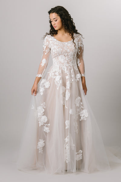 This modest wedding gown features long sleeves with lace decals throughout the bodice, skirt, and sleeves.