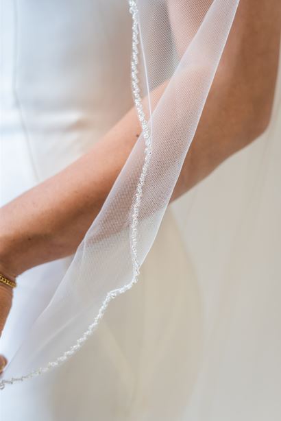 A close up shot of the beaded edge of a chapel length, scalloped edge bridal veil. This veil is perfect for adding some shimmer and beading to elevate any bridal look.