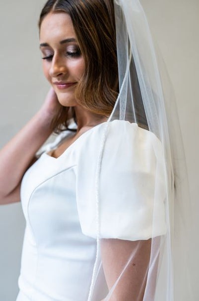 A side profile portrait shot of a bridal veil with white sparkly beading lining the entire edge of the veil. 