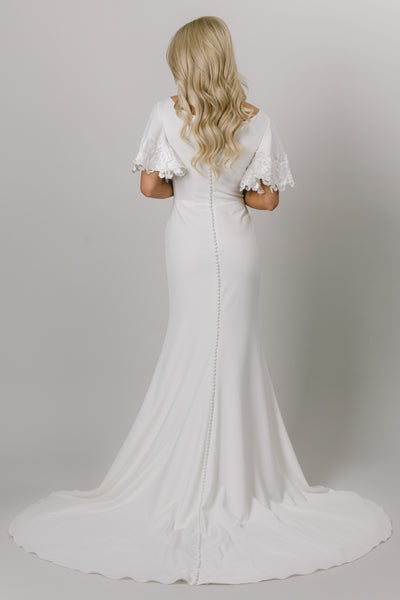 Back view of sleek and modern flutter sleeve gown. The flutter sleeves have lace on the edge. This modest wedding dress is fitted and has a v-neckline. Moments Made Bridal loves this elegant modest wedding dress.