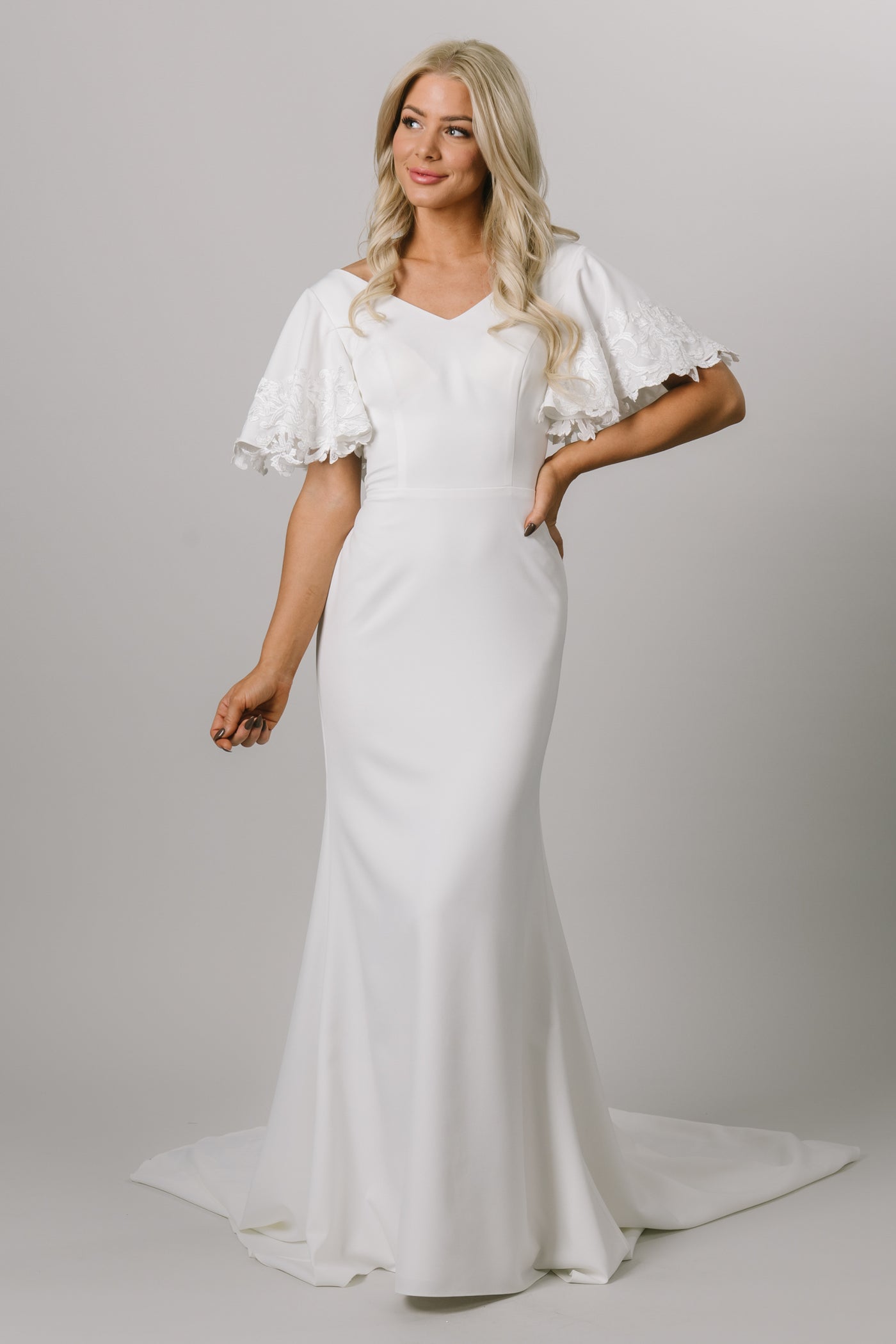Sleek and modern flutter sleeve gown. The flutter sleeves have lace on the edge. This modest wedding dress is fitted and has a v-neckline. Moments Made Bridal loves this elegant modest wedding dress.