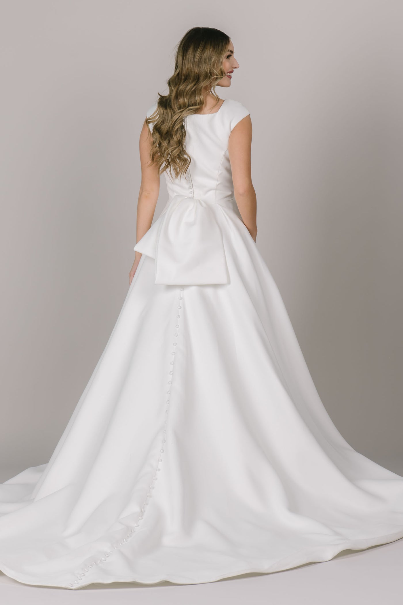 A back angle of a beautiful modest wedding dress in Bluffdale, UT with a bow, buttons going all the way down the gown, and a stunning square neckline.