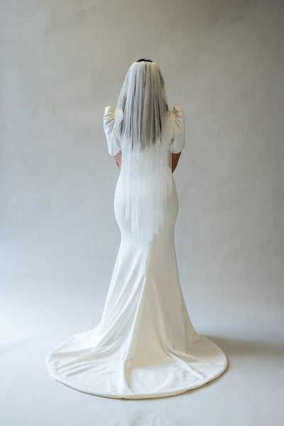 A back view full body shot of a fingertip length English netting simple veil. The perfect soft and flowy veil to add to any bridal look.