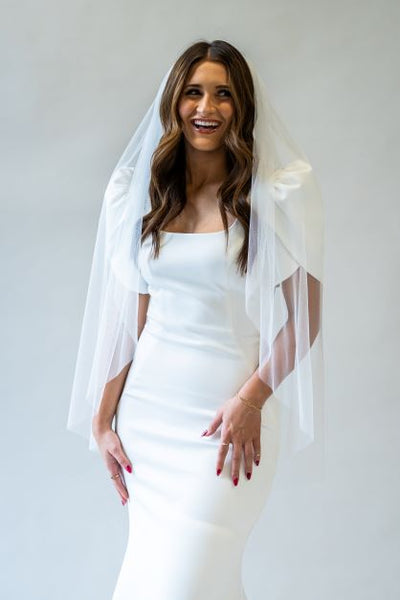A portrait of a English netting fingertip length bridal veil draping softly over the sleeves of a wedding gown.