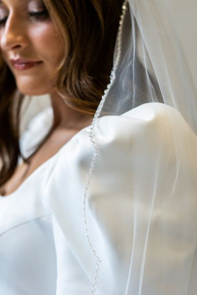 A close up side profile shot of a scalloped edge bridal veil with crystal beading lining the edge of the entire veil.