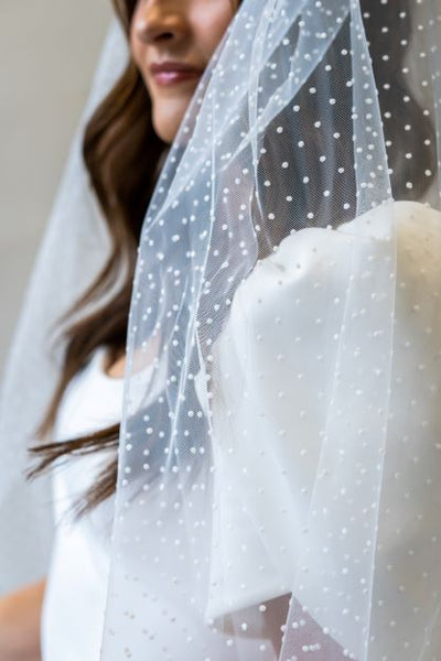 A close up shot of a swiss dot veil hanging over the puff sleeve of a simple wedding dress.