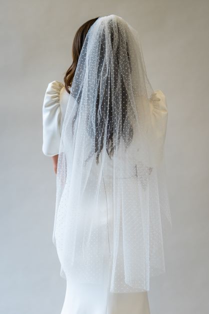 A portrait shot of the back of a model wearing a fingertip length swiss dot veil flowing over the back of a wedding dress. 
