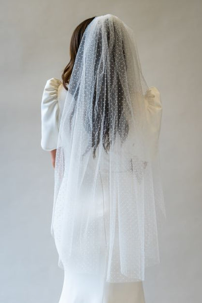 A portrait shot of the back of a model wearing a fingertip length swiss dot veil flowing over the back of a wedding dress. 