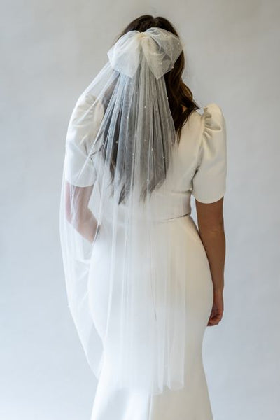 A back view portrait shot of a fingertip length bow veil with elegant pearls scattered throughout. The veil flows beautifully over the back of the wedding gown.