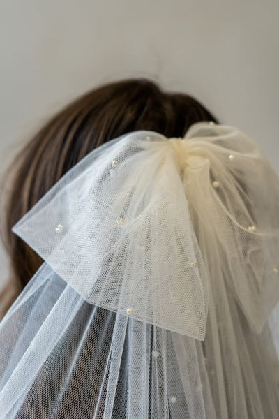 A close up shot of the back of a bridal bow veil with delicate pearls. It's made of English netting and hangs elegantly, adding a fun touch to the bride's hair.
