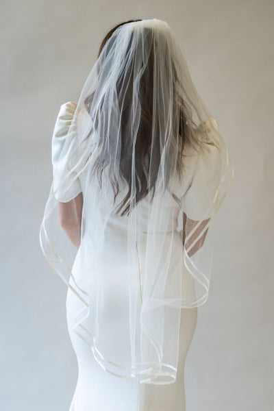 A portrait shot of the back of a fingertip length bridal veil with a double satin ribbon edge. The ribbon creates a wavy edge to the veil which creates a beautiful silhouette. 