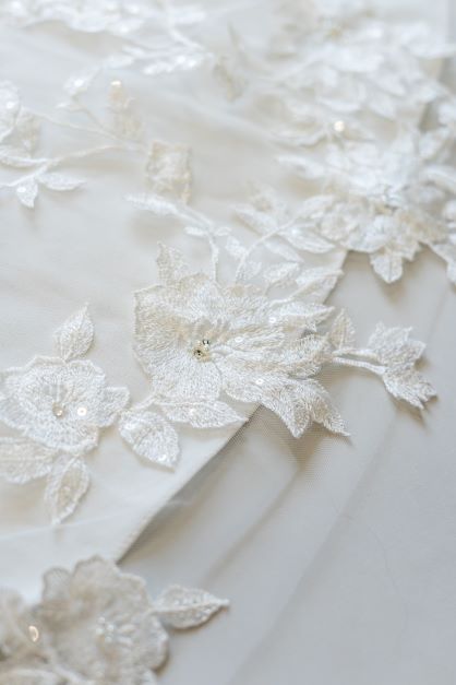 A close up shot of the detailed lace and beading on the edge of a cathedral length bridal veil. The lace has a floral focused design with leaves.