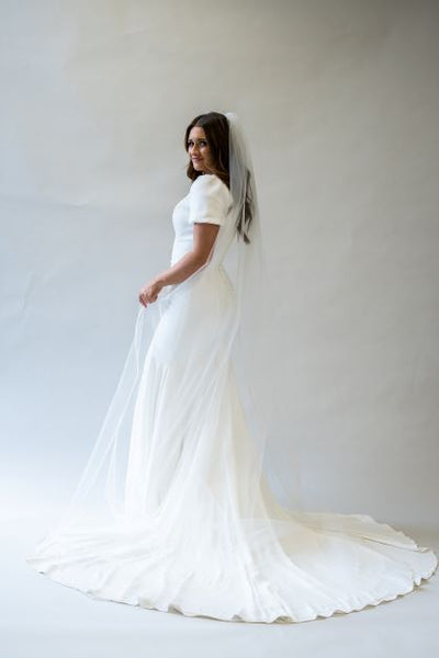 A side profile full body shot of a floor length simple bridal veil. The edge of the veil is lined with gorgeous white beading.