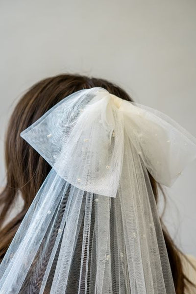 A close up shot of a bow veil with delicate pearls. It's the perfect accessory to add a fun touch to bridal hair and add elegance to your whole bridal look.
