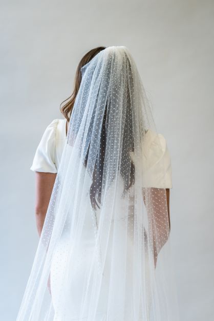 A back view, portrait shot of a swiss dot floor length bridal veil, draping down the back of a wedding gown. This veil is perfect for adding a fun touch to bridal hair and the back of a wedding dress.