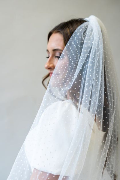 A close up side profile shot of a swiss dot floor length bridal veil draping over the sleeve of a simple bridal gown. 