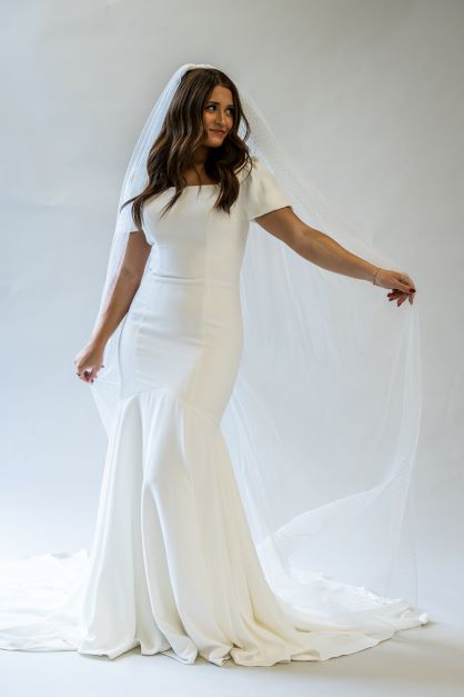 A front view, full body shot of a floor length swiss dot bridal veil being held to the side to show the length and gorgeous pattern.