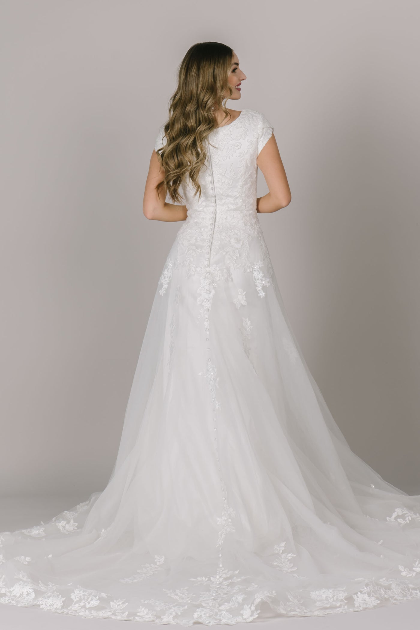 A back shot of an ivory modest wedding dress in Utah with buttons the go all the way down the gown, cap sleeves and a scoop back neckline.