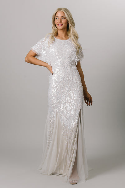 Front view of modest wedding dress with flutter sleeves. This Moments Made wedding dress has a fitted silhouette and tulle bottom. It has beading all over the dress. This dress looks good on all body types.