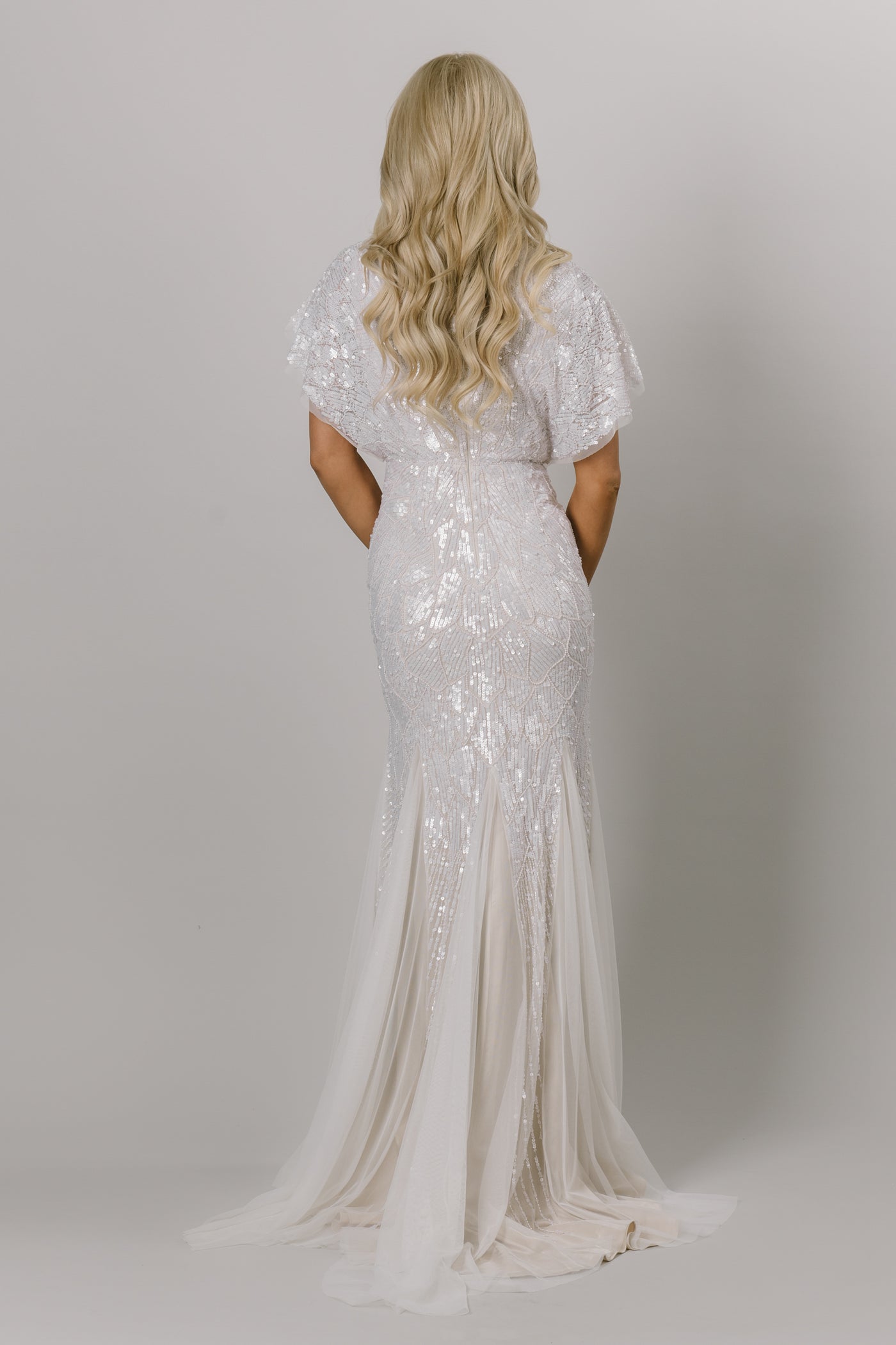 Back view of modest wedding dress with flutter sleeves. This Moments Made wedding dress has a fitted silhouette and tulle bottom. It has beading all over the dress. This dress looks good on all body types.