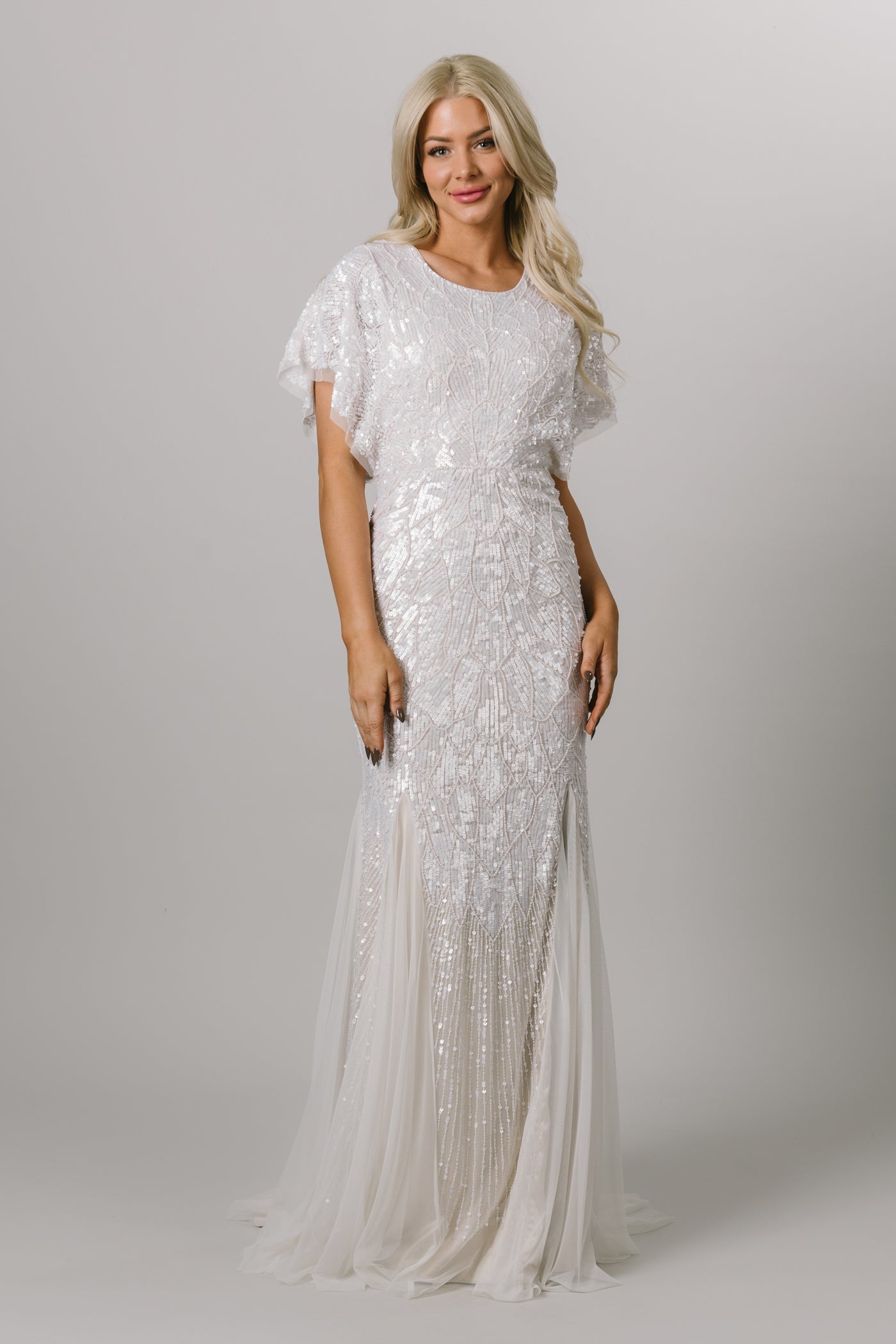 Front view of modest wedding dress with flutter sleeves. This Moments Made wedding dress has a fitted silhouette and tulle bottom. It has beading all over the dress. This dress looks good on all body types. 